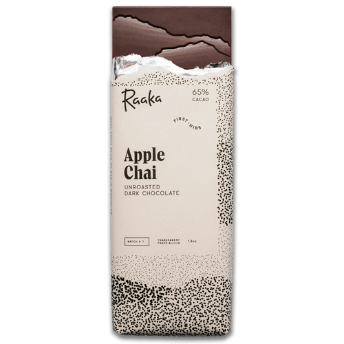 A vertical pack of Raaka Apple Chai unroasted dark chocolate bars, featuring a cream-colored wrapper with black text and speckled patterns, and a dark chocolate bar broken at the top, on a plain white background.