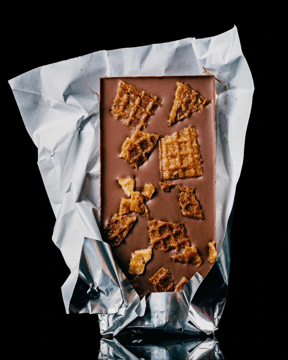 Chocolate Sundae and Cones bar with waffle cone pieces embedded in the center, presented inside it's silver foil against a black background.