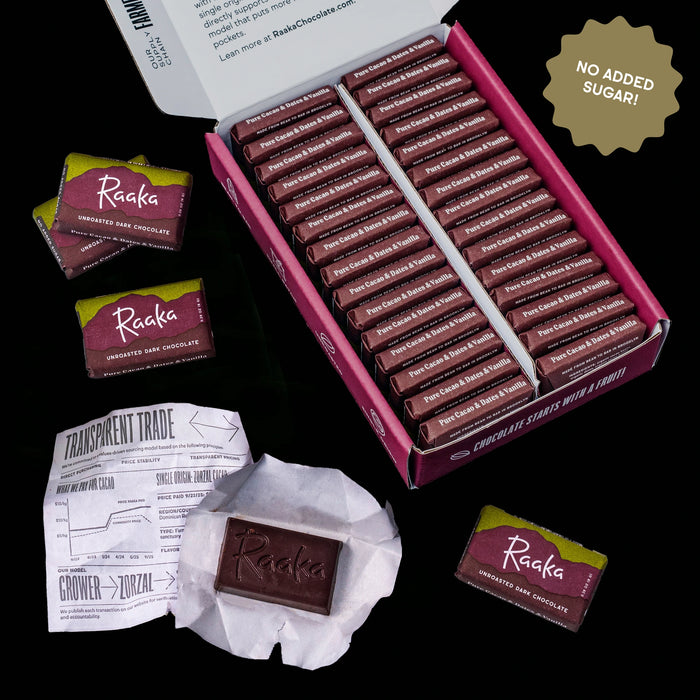 An open pink Raaka chocolate box filled with individually wrapped Pure Cacao & Dates & Vanilla-flavored chocolate bars, shown on a black background with a few loose packs and a wrapped bar beside it. A gold badge reads 'NO ADDED SUGAR!'.