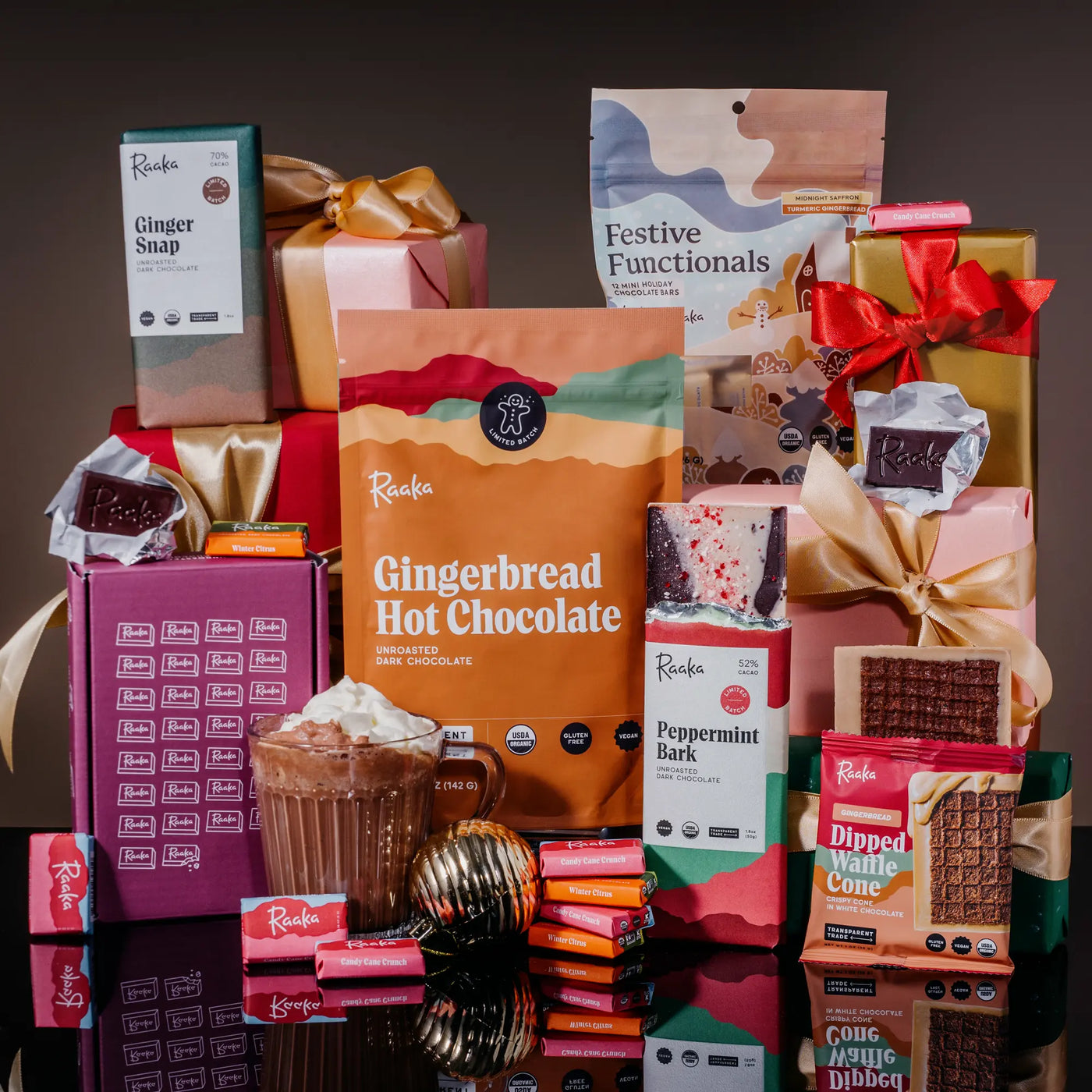 Raaka Holiday Products stacked with gift wrapped boxes. Peppermint Bark. Gingerbread Hot Chocolate. Ginger Snap. Mini bars.