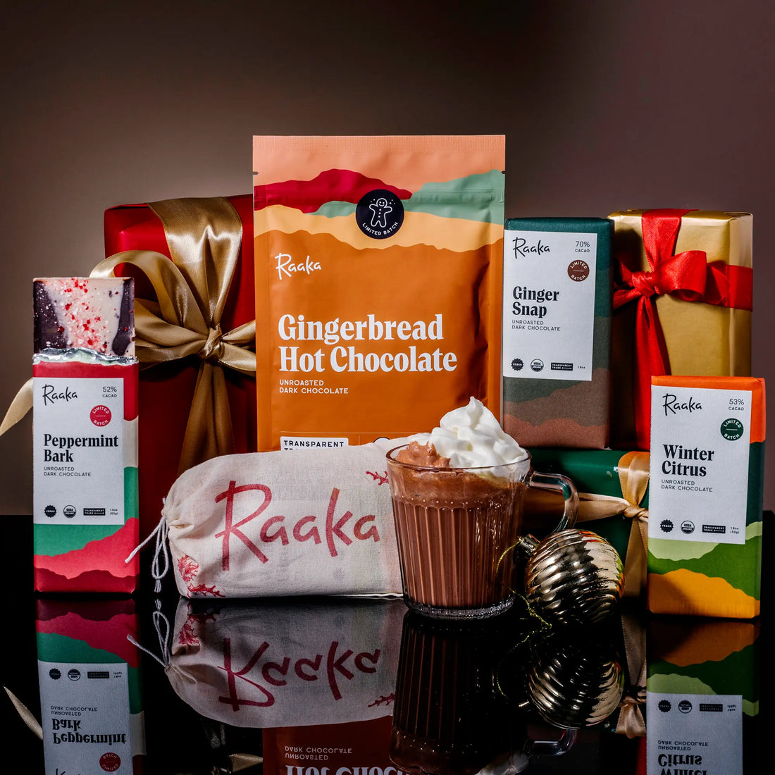 Raaka Holiday Bundle products including gingerbread hot chocolate, ginger snap, peppermint bark, and winter citrus with a glass of hot chocolate.