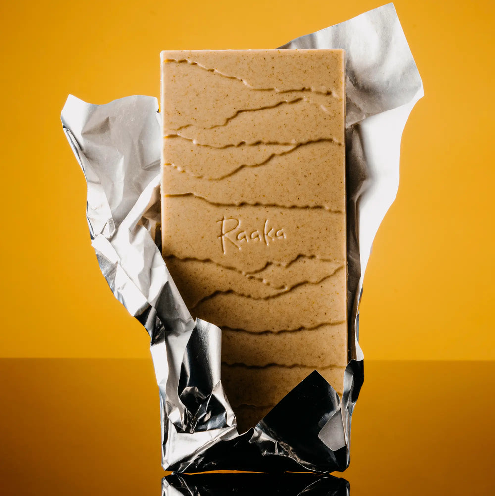 Raaka Lemon Tart bar open in foil, no paper wrapper, on yellow background.