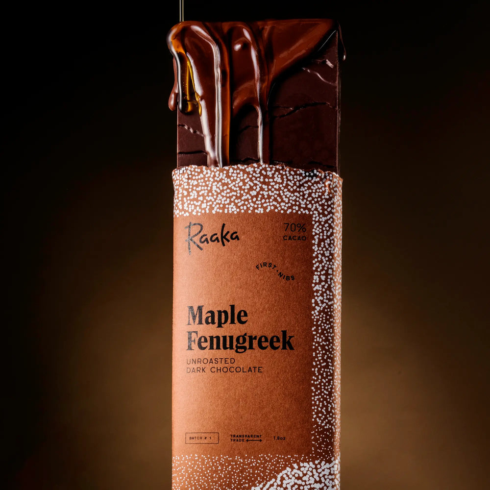 Maple Fenugreek dark chocolate bar with Raaka branding on a dark background. Maple syrup dripping on bar.
