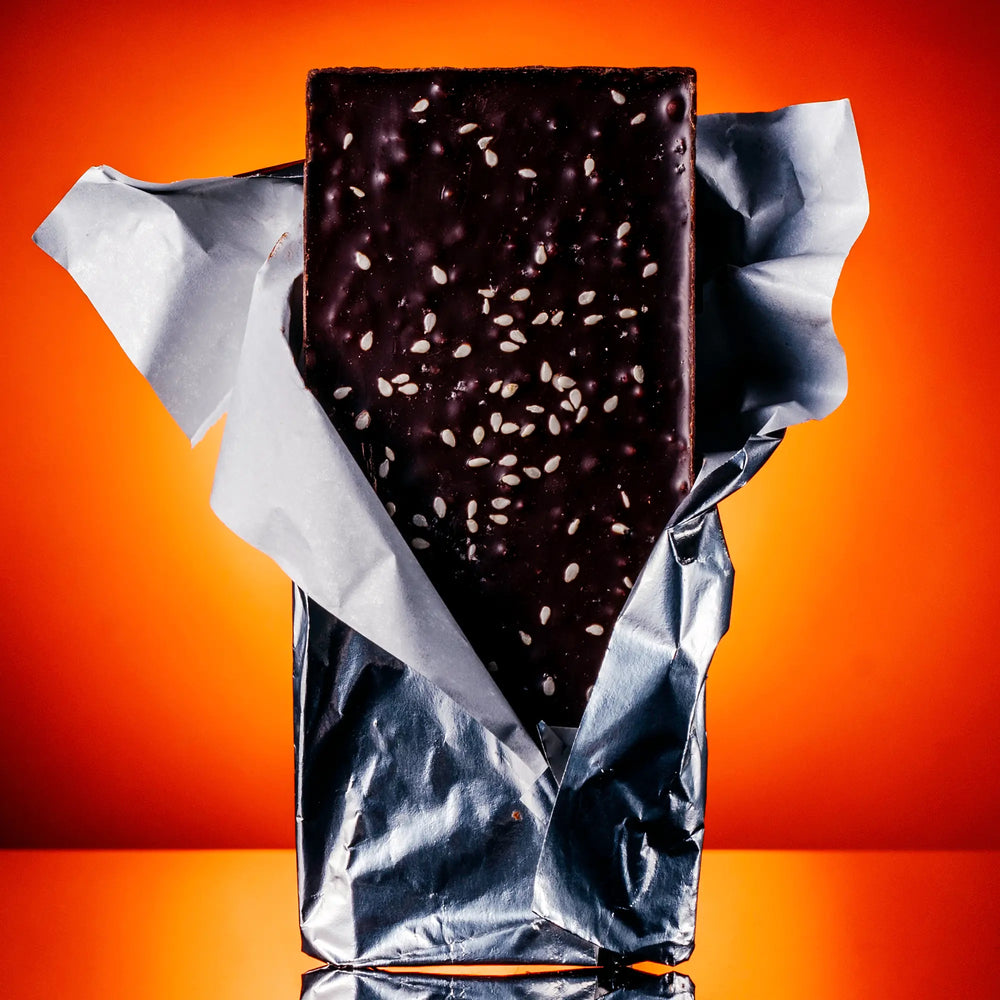 Back of the Chili Chocolate Crunch bar popping out of just the foil. Bar is garnished with salt and sesame seeds and has puffed quinoa. 
