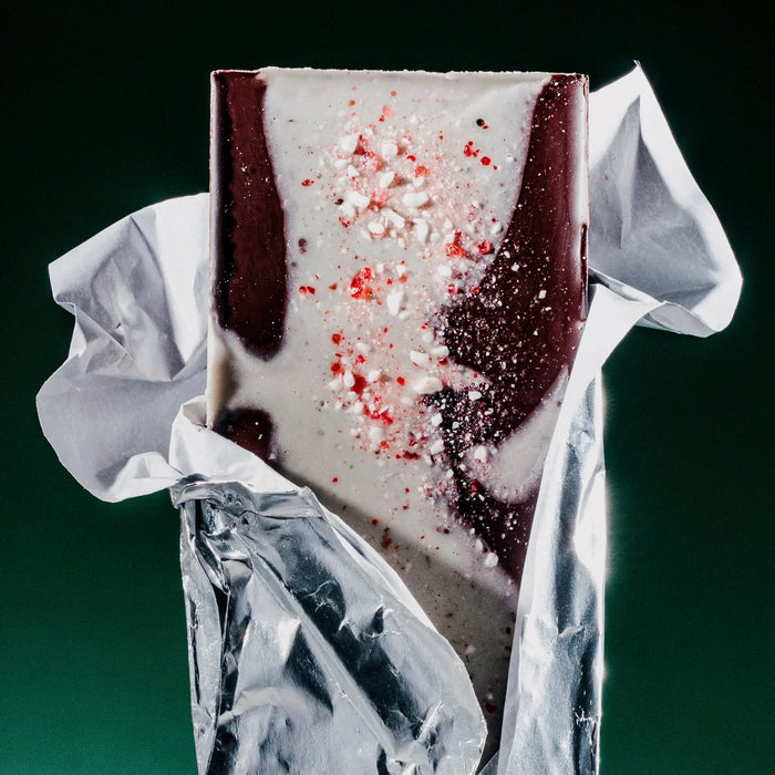 Peppermint Bark bar popping out of wrapper. White chocolate layered on top of dark chocolate, garnished with candy canes.