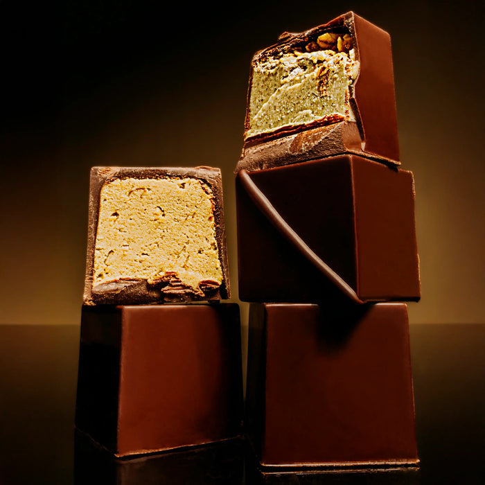 Six seed butter praline cubes stacked on a dark background. Two are cut open to reveal a nougat-like center.