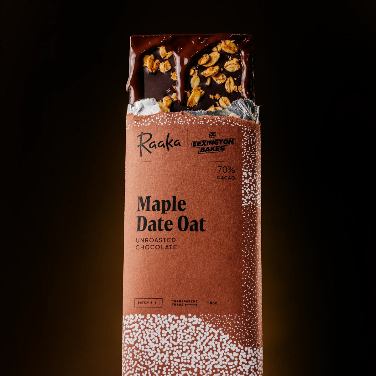 A wrapped chocolate bar of Raaka and Lexington Bakes's Maple Date Oat' on a dark background, with the wrapper showing a partially unwrapped section at the top revealing dark chocolate and oat crisp topping.