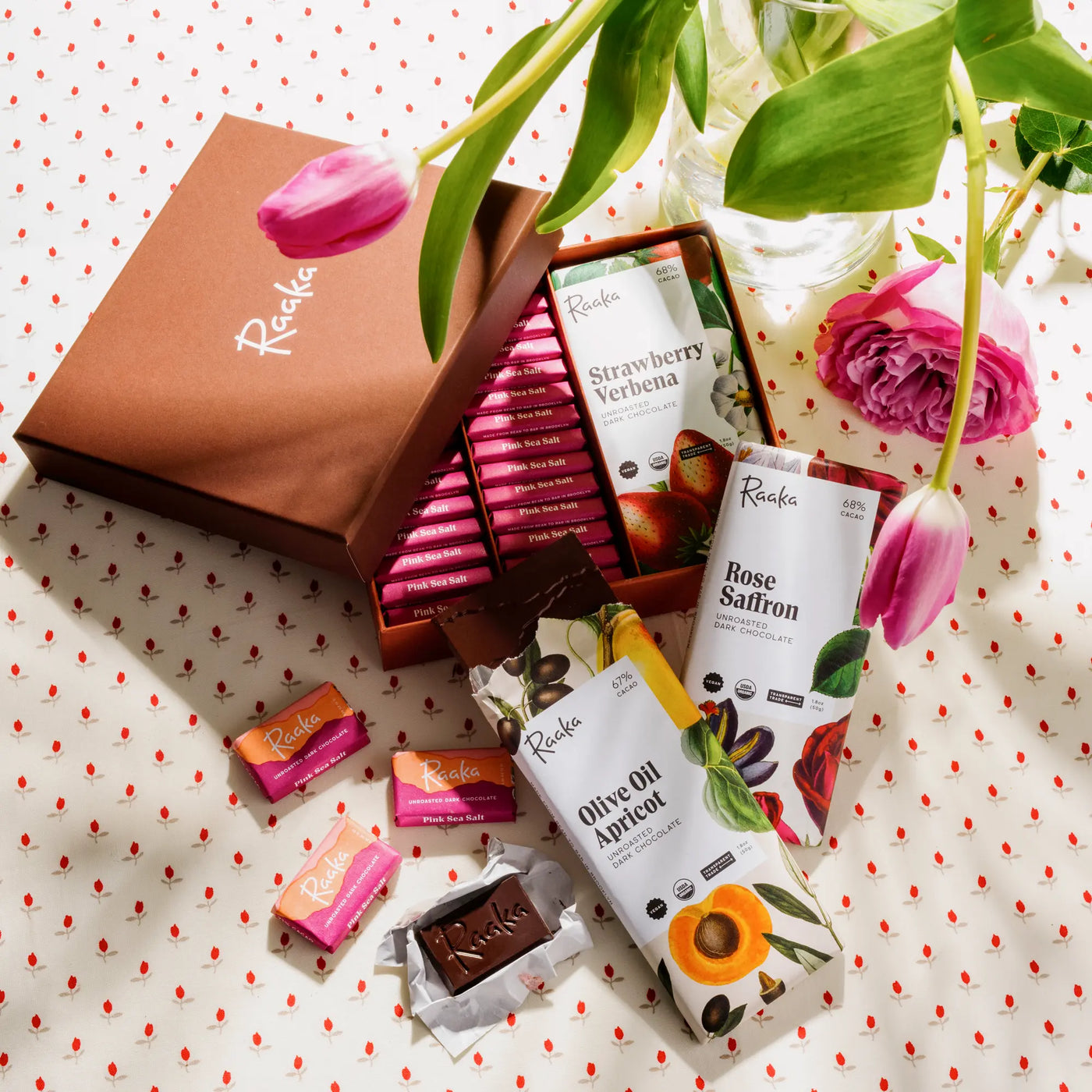 Assorted chocolate bars from Raaka on a polka dot surface with flowers.