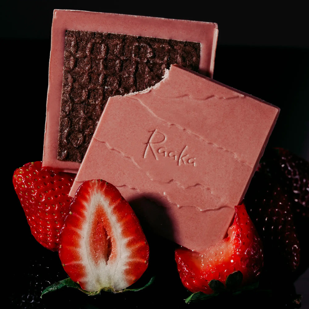 Open pieces of Strawberry Dipped Waffle Cone propped up on strawberries. Chocolate bar is pink with a dark cocoa waffle cookie on top.