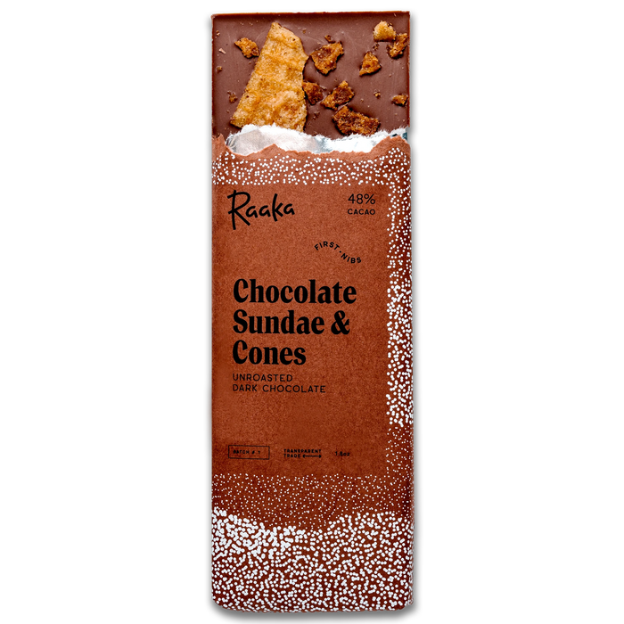 A packaged chocolate bar labeled 'Raaka Chocolate Sundae & Cones' on a plain white background. The wrapper is predominantly brown with white speckled edges and shows a partially unwrapped dark chocolate bar at the top with cookie pieces embedded in it.