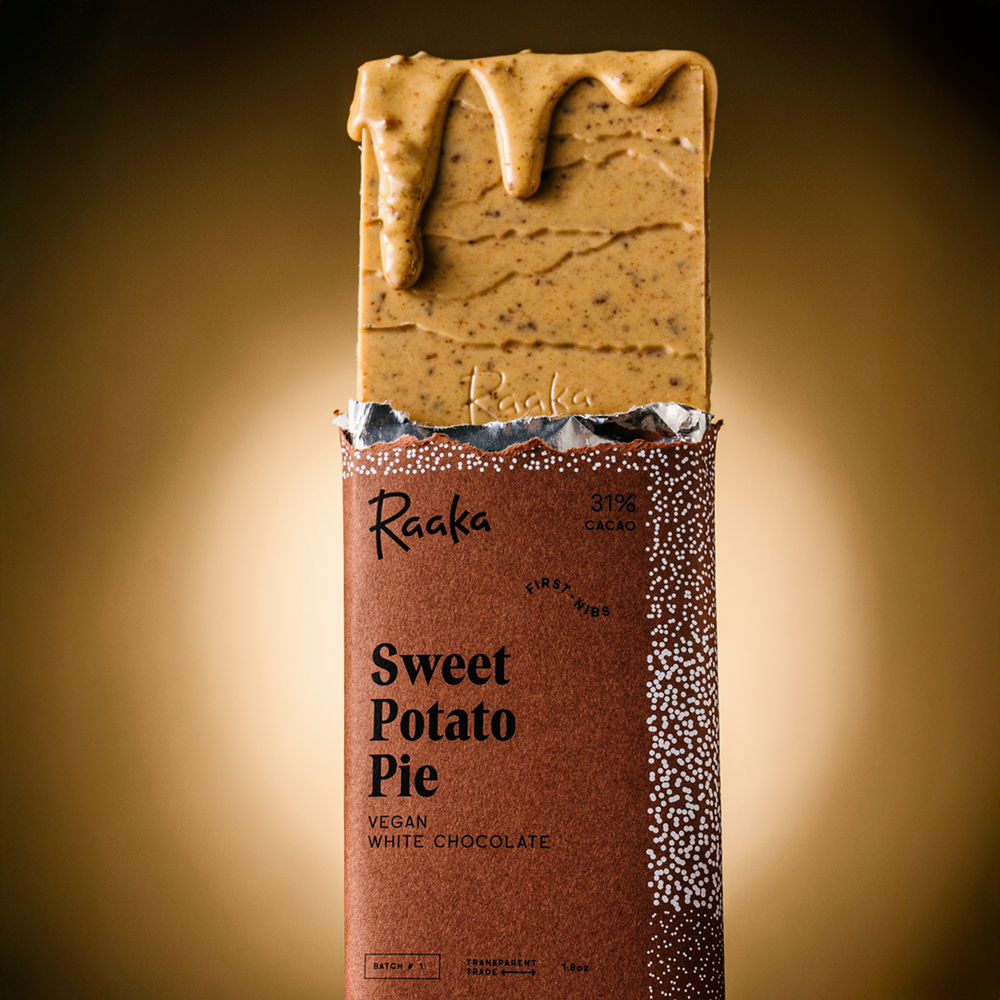 Sweet Potato Pie bar popping out wrapper, with a melty drip of chocolte. Bar is orange tinted and filled with bits of pumpkin spice cookies.