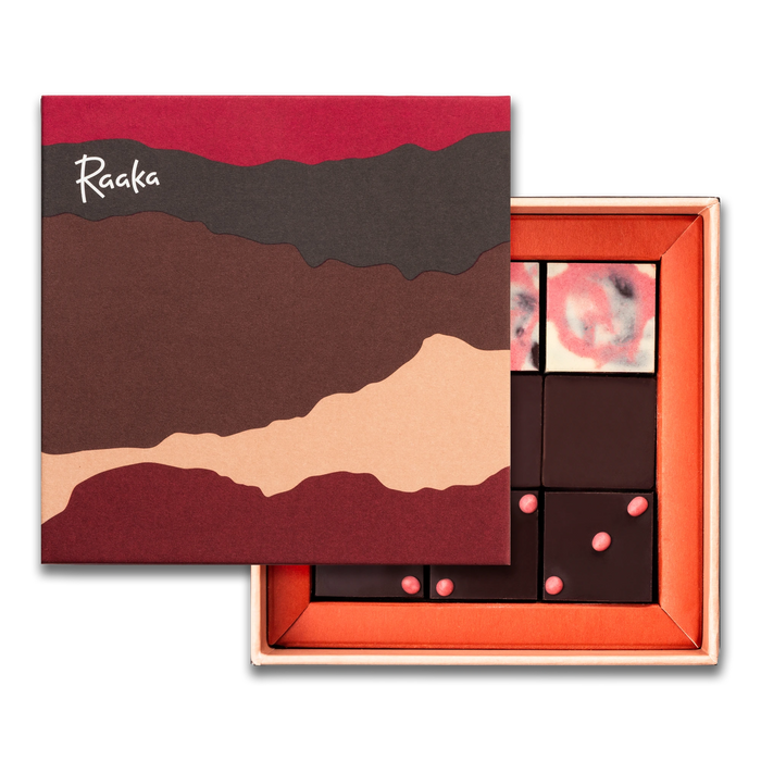 Open box of chocolates with a decorative lid featuring the brand 'Raaka'.
