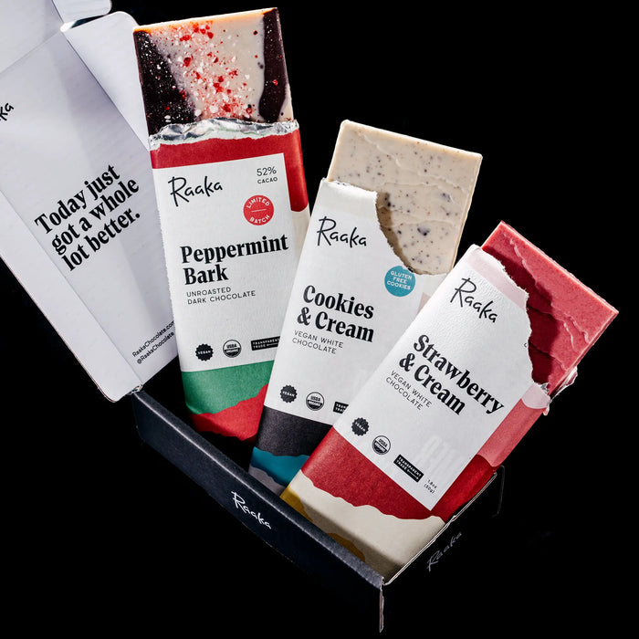 Three Raaka white chocolate bars in a black box: Peppermint Bark, Cookies & Cream, and Strawberry & Cream.