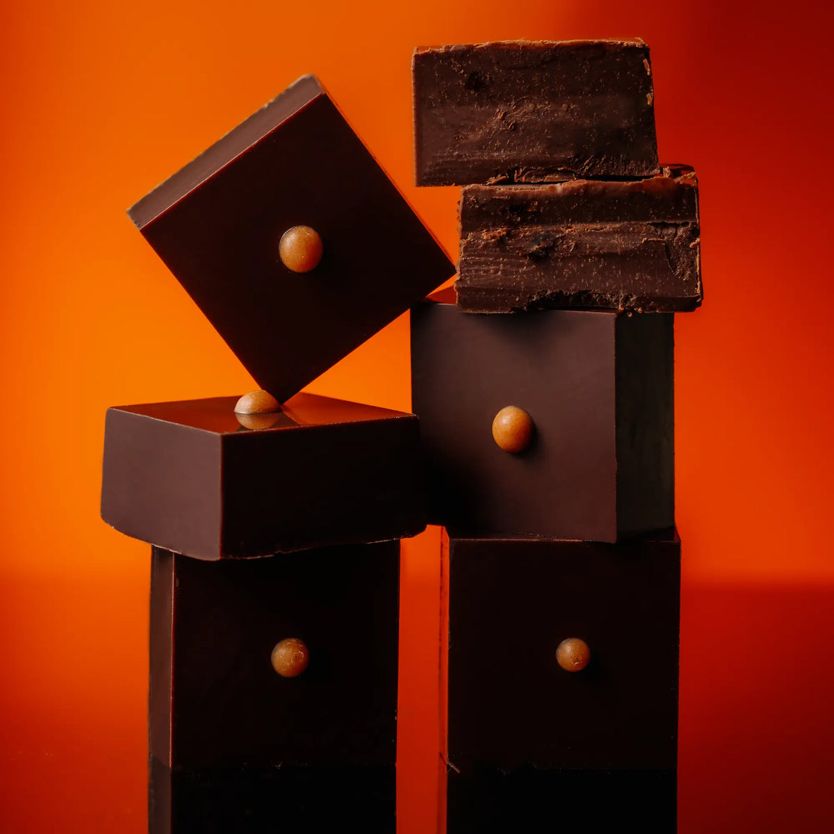 A stack of dark chocolate meltaway truffles with chili-infused olive oil on a firey orange red background.