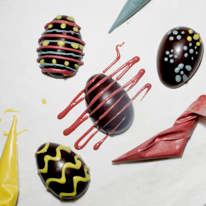 Three decorated chocolate eggs surrounded by decorating tools.