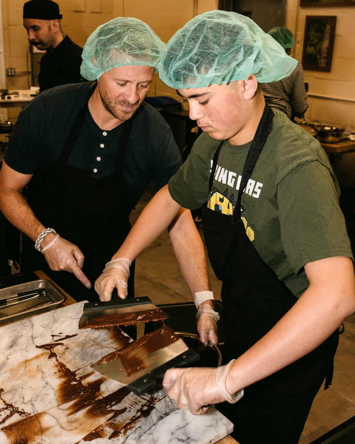 An adult man and and young boy scraping chocolate into a bowl 